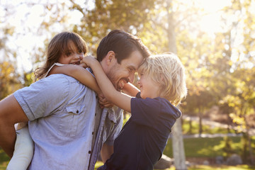 Fototapeta premium Father Carrying Son And Daughter As They Play In Park