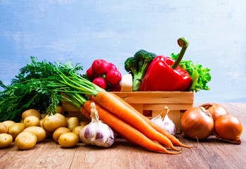 Vegetables. Potatoes, carrot and red pepper. Garlic, onion and brocoli. Lettuce salad and red radish. Wooden basket on blue background.