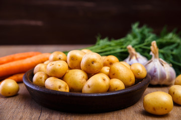 Potatoes in plate. Carrot, garlic and raw new potato. Fresh natural vegetables. Organic bio food on rustic wooden table.