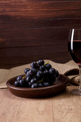 Red wine. Wineglass with dark grapes branch on plate. On rustic wooden background.