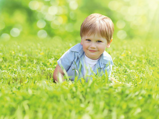 Portrait cute smiling child playing lying on grass in sunny summer day over blurred background