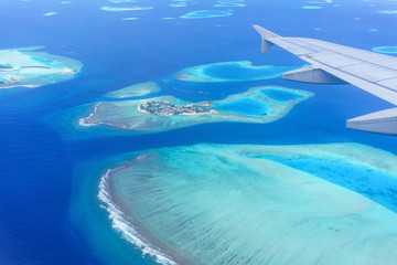 Scenery from airplane 's window seeing wing of airplane , white clouds , blue sky and Maldives islands