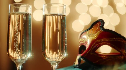 Two glasses filled with bubbly champagne and carnival masquerade mask. Bokeh lights on the background