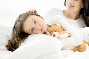 Adorable daughter and mother lying and relaxing on bed at home