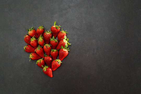 Zu einem Herz angeordnete Erdbeeren auf dunkelrauer Schieferplatte mit Platz für Text auf der rechten Seite