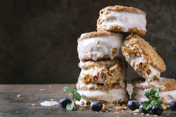 Set of homemade ice cream sandwiches in oat cookies with almond sugar crumbs, blueberries and mint over dark metal texture background. Close up