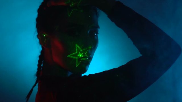 Sexy woman model with posing at smokey studio with laser light effects on her face over blue glowing background - video in fast motion