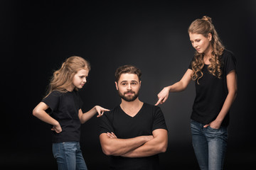 mother and daughter quarreling at father sitting with crossed arms on black