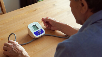 BACK VIEW: Elderly man measuring the blood pressure at home