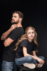 adorable pensive daughter and pensive father back to back on black