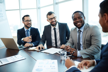 Joyful multiethnic group of managers analyzing results of accomplished project while gathered in boardroom, waist-up portrait