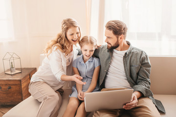 Happy family sitting on sofa and using laptop at home