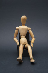Person represented by a wooden dummy relaxing while sitting on an armchair in a comfortable position.
