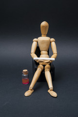 /Person represented by a wooden dummy sitting on an armchair and holding a cigarette with a bottle of alcoholic drink aside.