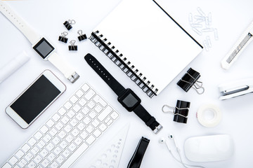 Flat lay of office supplies, keyboard, notepad, smartphone and smartwatches on white