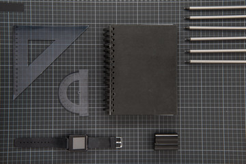 Flat lay of black office supplies, notepad, smartwatch and pencils on black blueprint