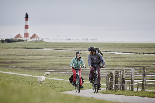 Germany, Schleswig-Holstein, Eiderstedt, couple riding bicycle near Westerheversand Lighthouse