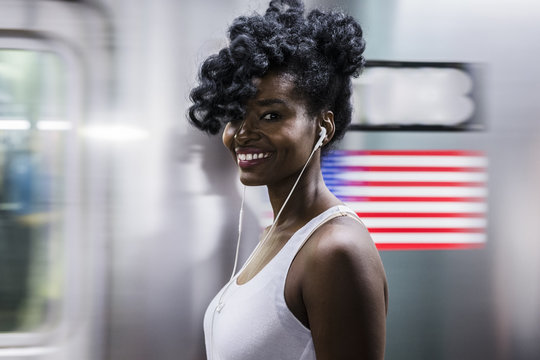 USA, New York City, Manhattan, portrait of happy woman with earphones on subway station platform