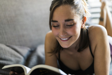 Smiling young woman in lingerie reading book on couch