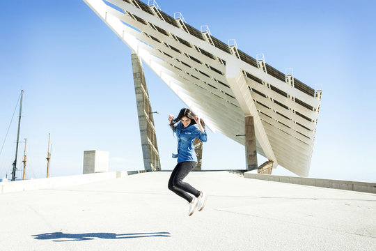 Young woman jumping in the air with solar panels in background