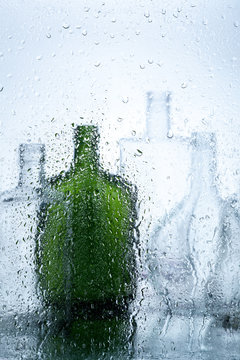 Still life of bottles behind wet glass on a light background.