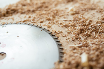 Metal blade of circular saw lying on wooden table with shavings, close-up shot