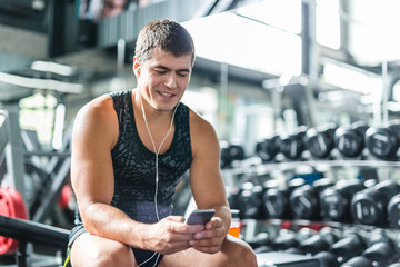 Portrait of strong muscular man  listening to music looking at  smartphone screen while sitting on...