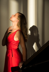 Portrait of elegant woman in red dress. Fashion Model Beautiful young Girl posing near the piano. Close up of young pretty blonde girl with close eyes.