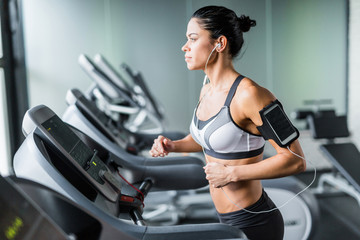 Portrait of sportive brunette woman exercising on treadmill in gym listening to music using...