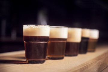 Several different beers are standing in a row at the bar in small mugs