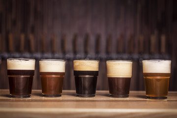 Several different beers are standing in a row at the bar in small mugs
