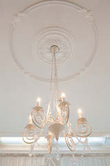 A view from below on a white chandelier hanging from a ceiling rose molding