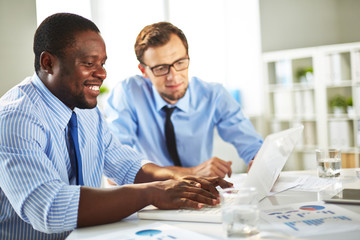 Collaborative work on new computer application: Afro-American programmer writing code on laptop while his superior giving guidance