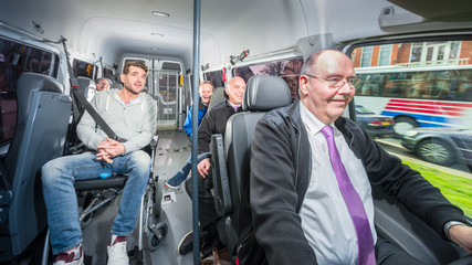 Group of people, travelling in a minivan with a busdriver and disabled person