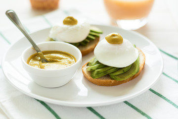 Vegetarian breakfast: avocado toast with poached eggs and mustard, orange juice,muffin on white wooden background. Selective focus