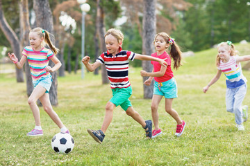 Elementary school kids in summer wear playing soccer on green lawn in park