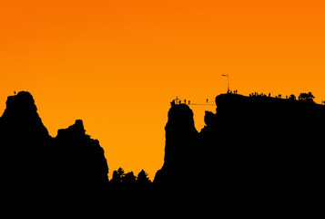 Obraz premium На вершине скалы по натянутому канату идет человек, толпа людей наблюдает за ним. Силуэт вершины скалы.