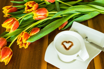 Greeting card with cup of coffee with heart and red tulips on the wooden background