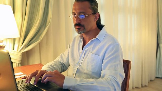 middle age attractive handsome man with glasses using laptop at home office
