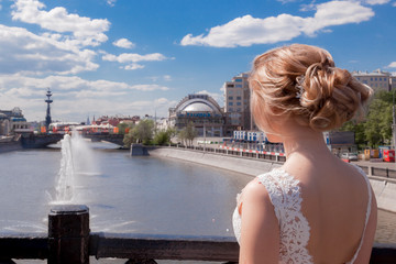 Fototapeta na wymiar bride standing in the city on the bridge watching the river blue sky clouds