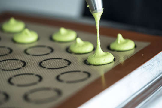 macarons being piped on to the mat