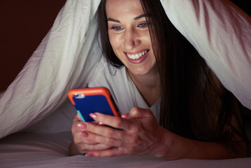 Girl under blanket at night with a smartphone