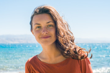 Fototapeta na wymiar Portrait of happy smiling young woman with long hair on the beach and sea background