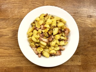 Roasted potato and bacon on a white plate and wood table from top view