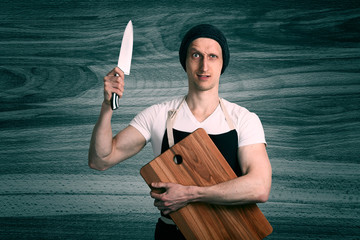 A chef with a large knife and wooden cutting board in his hands. Studio portrait closeup