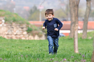 Happy boy play and running at park in spring. Little smiling kid play in city park.