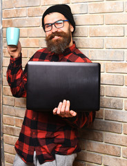 Bearded brutal caucasian hipster holding laptop with cup