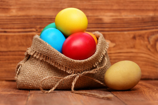 painted easter colorful eggs in burlap sack on wooden background