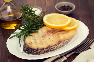grilled fish with lemon in white dish on wooden background