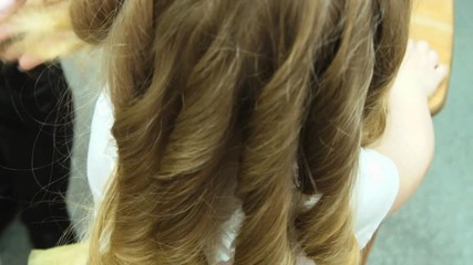 Little girl. The mother raises the girl's hair with a Curling iron. Preparing for a photo shoot. A beautiful child's face. Curly hair